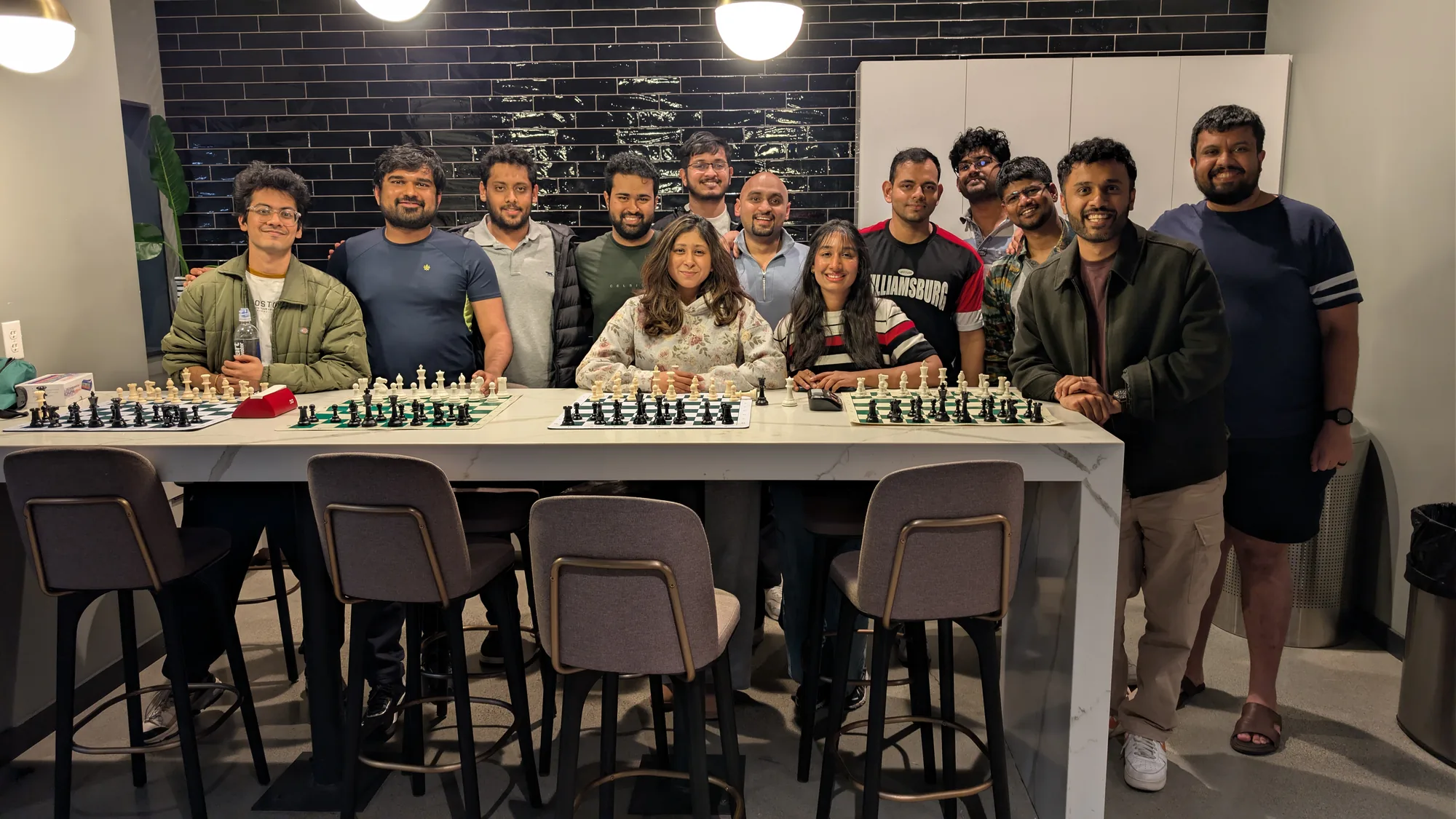 Fourteen club members standing and sitting behind a long table with four chess boards laid out on it.